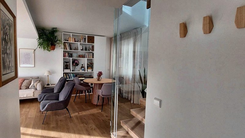 View from the hall into the living room with bookshelf and armchairs