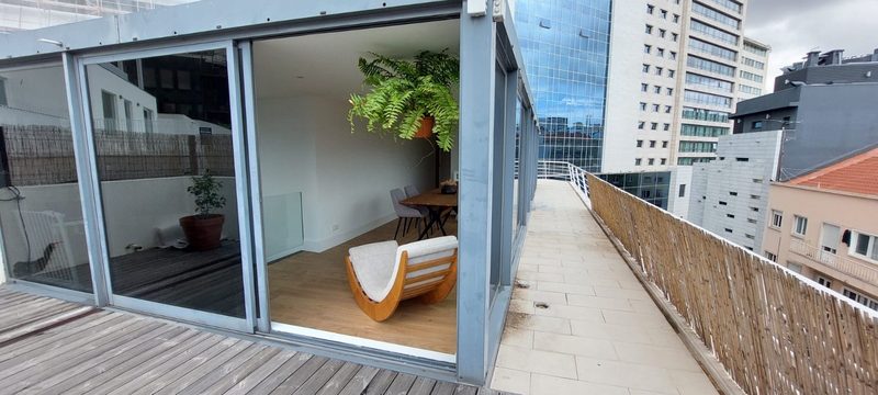 The glass-walled lounge seen from the wooden deck, with the terrace running along the building and office towers behind
