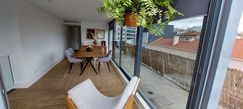 The lounge with the dining table, a hanging fern and a wall of sliding glass along the terrace