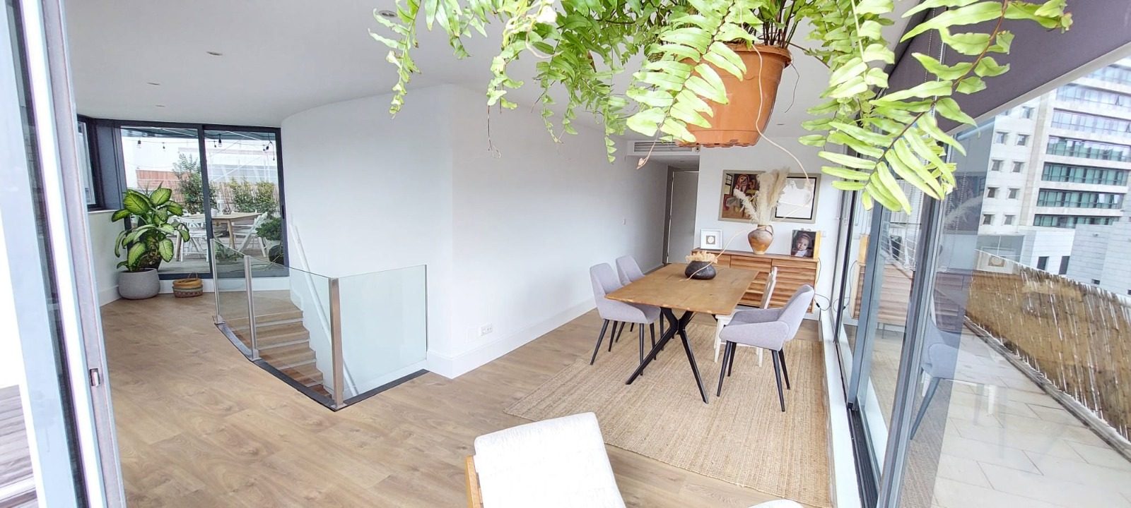 The upper lounge with the glass-railed staircase, a hanging fern and the dining table by the floor-to-ceiling windows