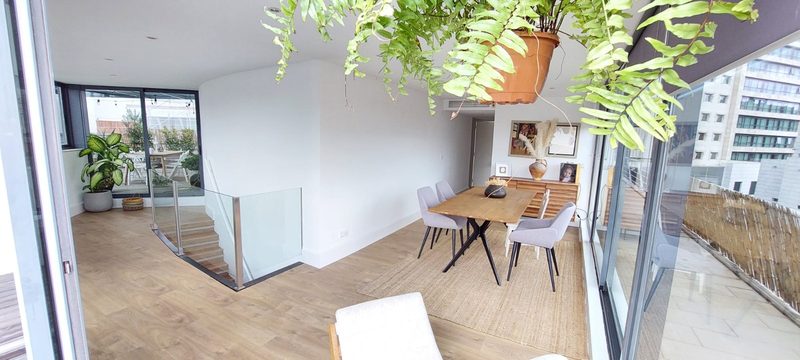 The upper lounge with the glass-railed staircase, a hanging fern and the dining table by the floor-to-ceiling windows