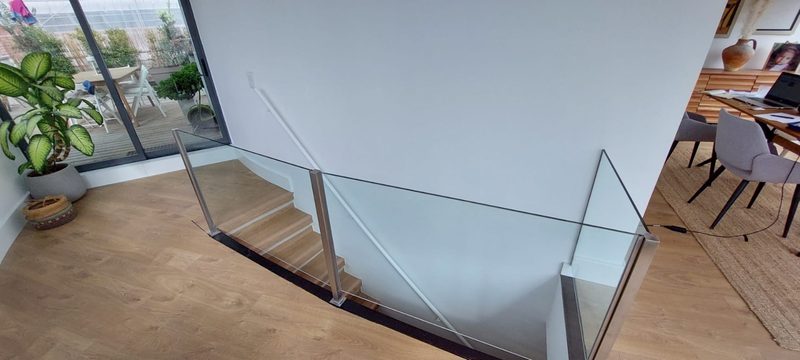 The glass-railed staircase down to the lower floor, with a work desk beside it and the terrace behind the glass