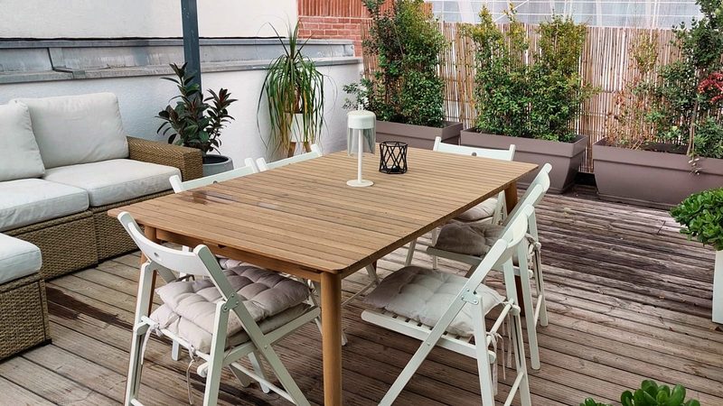 Dining table and outdoor sofa on the wooden deck of the upper terrace, with planters along a reed screen
